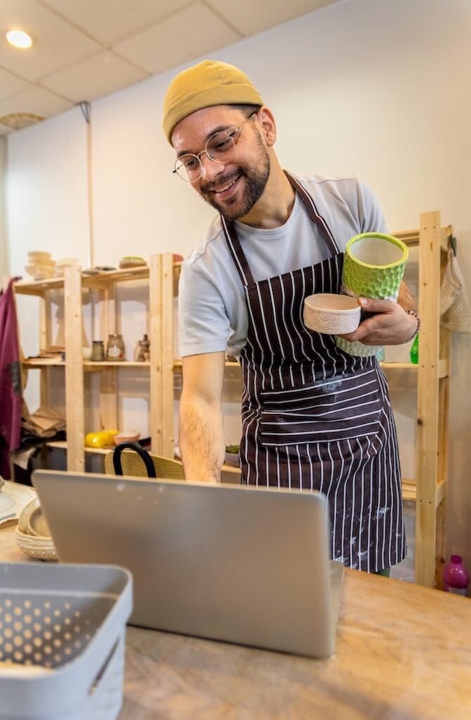 male business owner using laptop in pottery studio workshop.